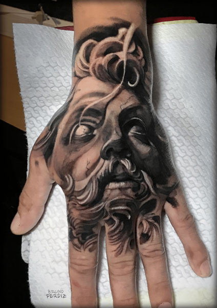 Marble face of Zeus tattooed on a hand.